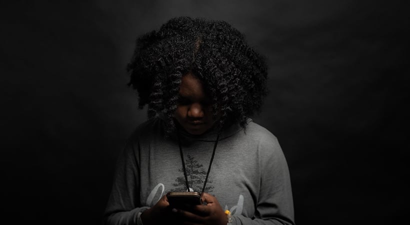 Concerned child in dark room looking at a mobile phone