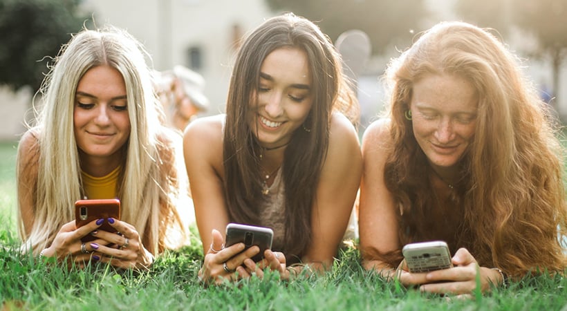 3 teenage girls lying down, smiling at their mobile phones